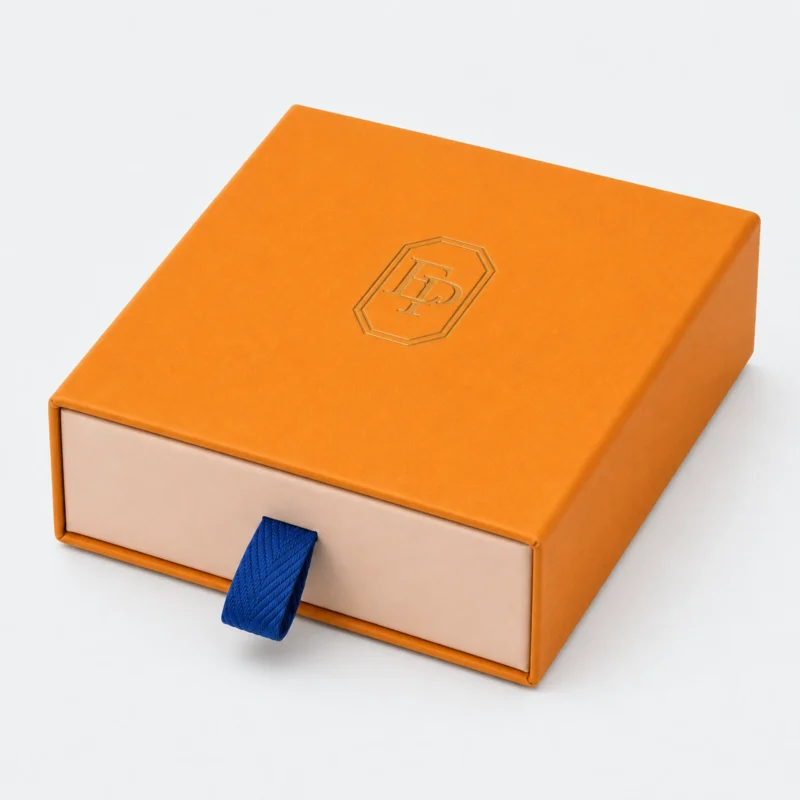 Closed orange paper drawer gift box with blue pull tab and gold logo