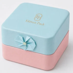 Gold logo and side paper flower on a pastel jewelry box with a clean closure seam