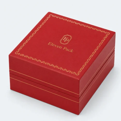 Closed red leather watch box with gold logo and decorative lid border