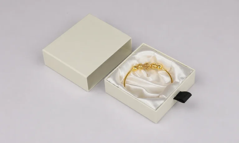 Ivory drawer jewelry box with a satin-lined tray and gold bracelet beside its unbranded sleeve.