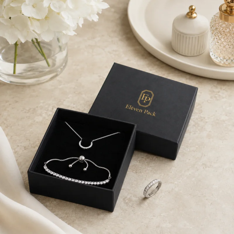 Black jewelry box displaying necklace and bracelet pieces in a styled packaging scene