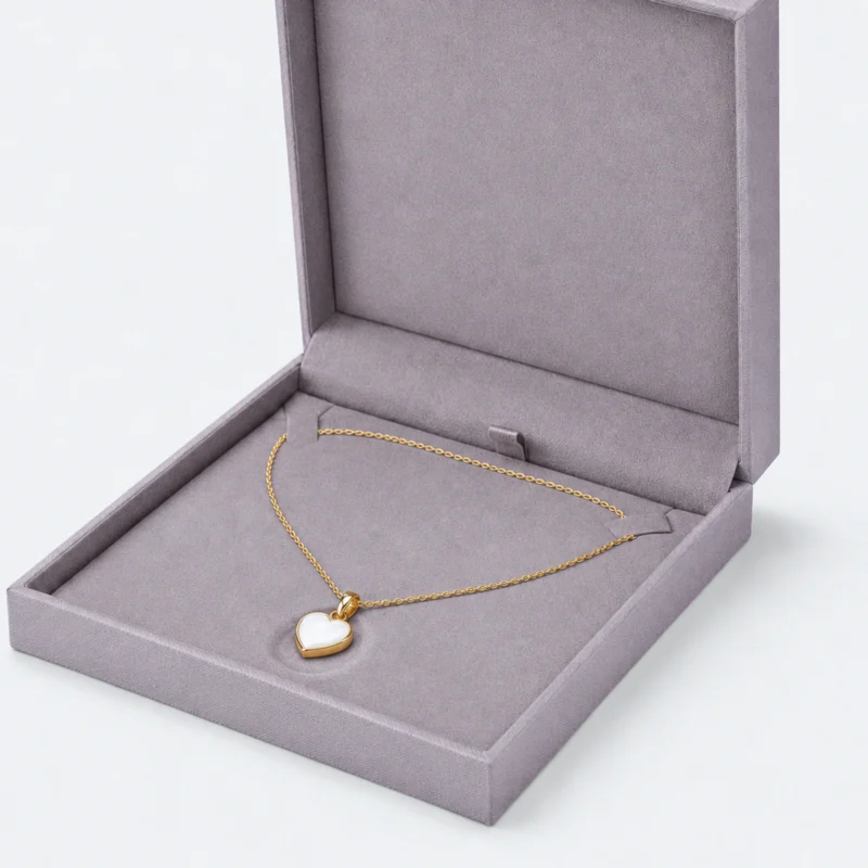 Close-up of two necklace tabs and heart pendant resting in a shallow padded recess