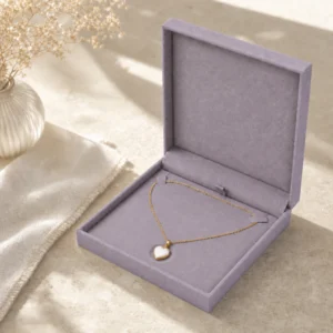 Gray lilac linen necklace box with consistent heart pendant support in sunlight